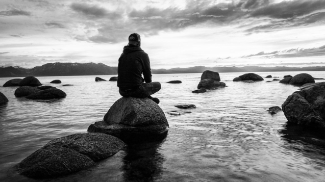 Man sitting on a rock by a lake meditating