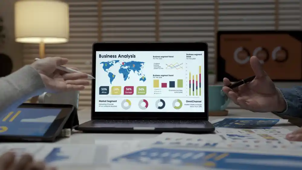 Two people, with only their hands showing, in front of a laptop that has graphs and map, discussing the enterprise SEO analytics of a tech company