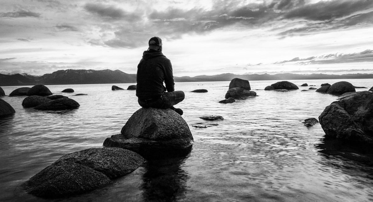 Man sitting on a rock by a lake meditating